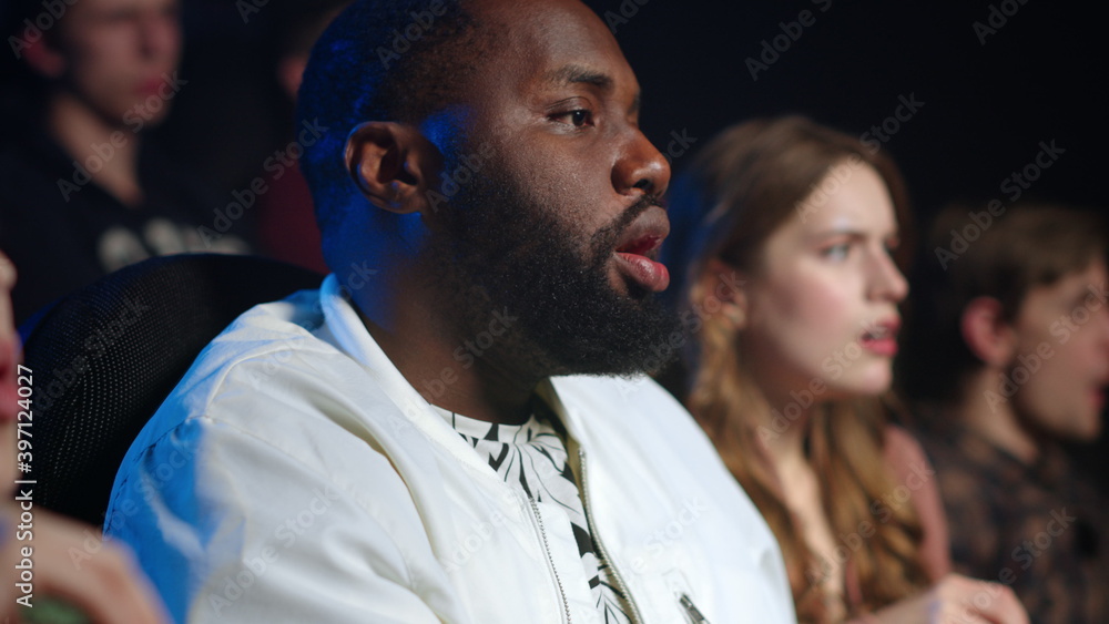 Multicultural people eating popcorn in cinema. Worried african man watching film. Multicultural people eating popcorn in cinema. Worried african man watching film.