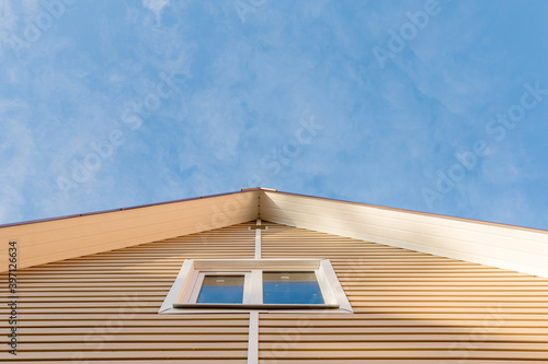 The facade of the new house clad with siding, with windows, against the blue sky.