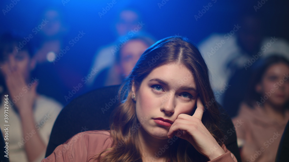 Frustrated woman watching boring movie. Upset girl yawning in movie theater.