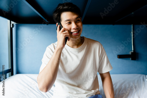 Asian man talking on the phone in dormitory bed room.