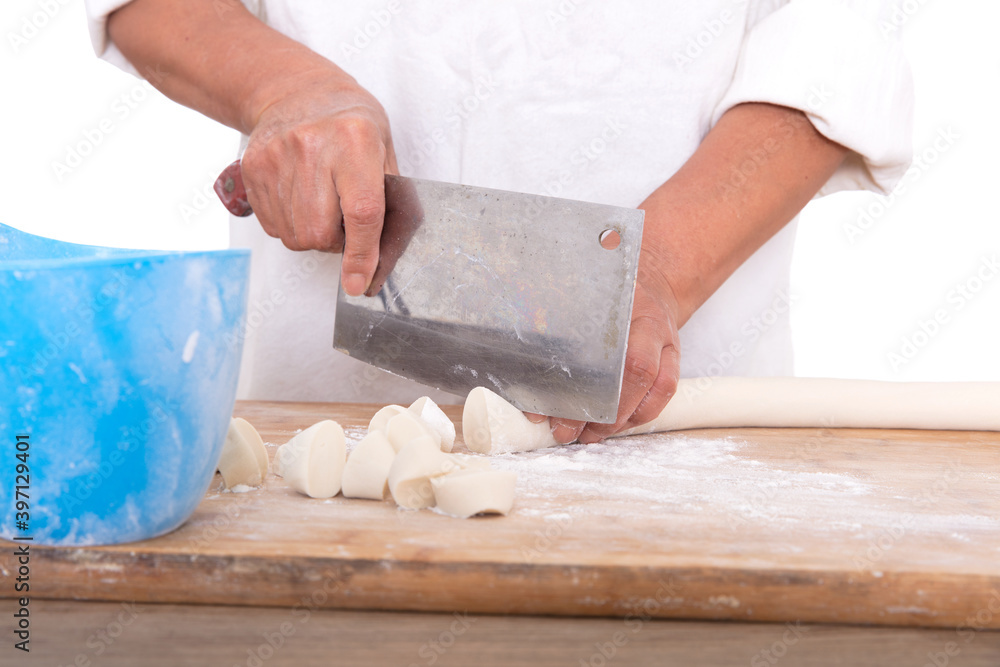 The pastry chef cuts the long white dough into small dough with a kitchen knife The pastry chef cuts the long white dough into small dough with a kitchen knife