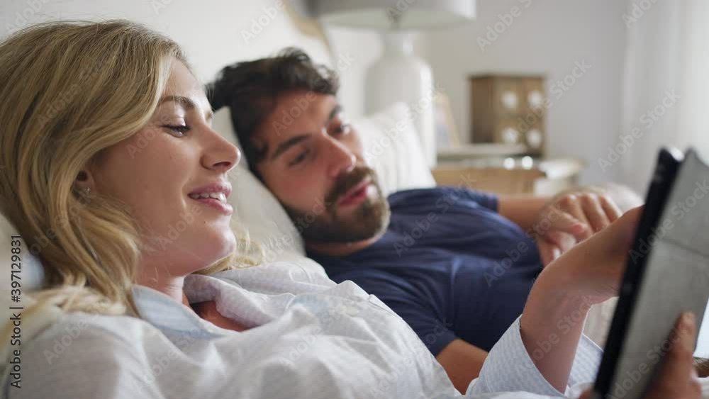 Couple lying in bed in morning looking at digital tablet together - shot in slow motion Couple lying in bed in morning looking at digital tablet together - shot in slow motion