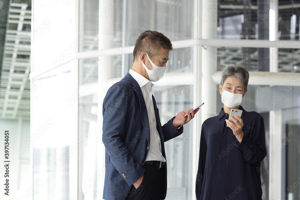スマートフォンを見るマスクをつけたシニア世代ビジネスマンとビジネスウーマン
