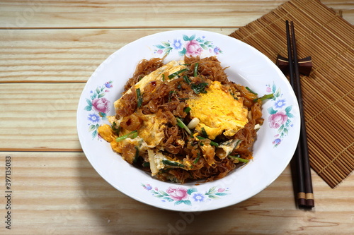 Fried and stirred spicy rice noodle mixed with local sauce, scrambled egg and cutting spring onion serving on the plate. Famous traditional noodle menu in Asia restaurant. 