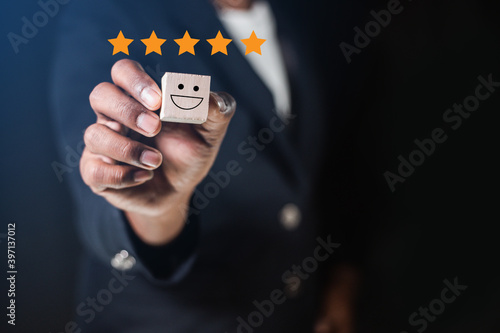 A businessman picks up a wooden block with a smiley face icon and five stars. Concept of customer satisfaction