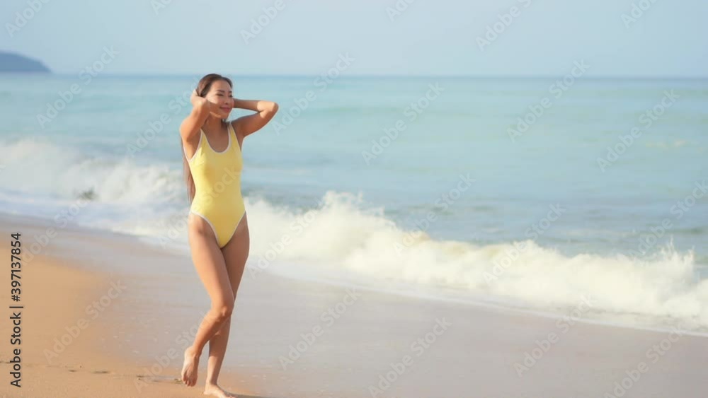 A pretty young woman in a yellow bathing suit walks along the shore welcoming the incoming waves. A pretty young woman in a yellow bathing suit walks along the shore welcoming the incoming waves.
