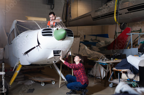 Ordinary male aircraft enthusiast with female assistant working in workshop on creating of light aircraft flying model