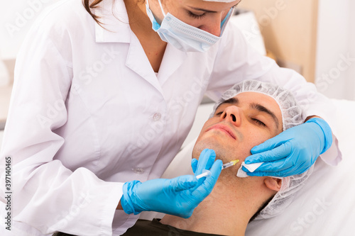 Confident woman doctor giving injections with syringe for facial correction to male patient in clinic of aesthetic medicine