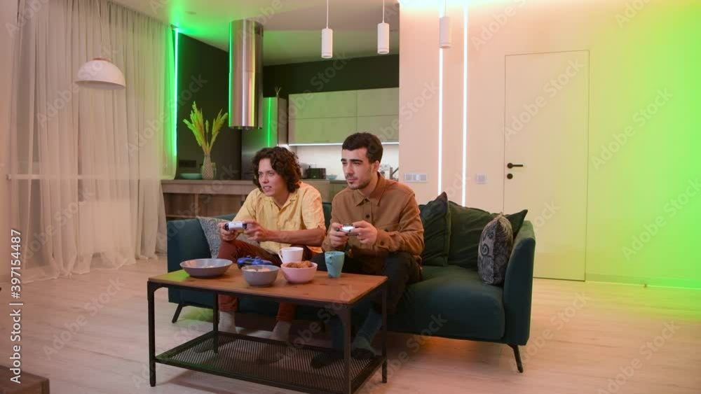 Happy male gamers playing video games at home. Winning in a battle congratulate each other with victory. Guy with manicure holding gaming console joystick.
