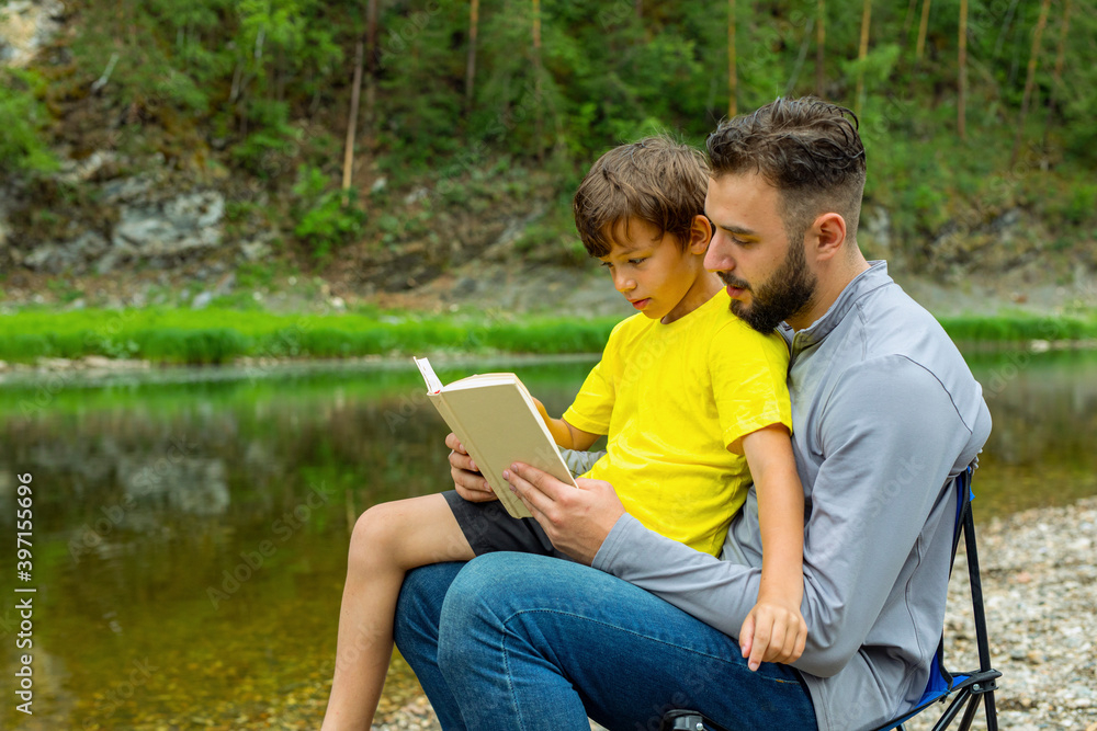Daddy with kid reading book sitting by river or lake Daddy with kid reading book sitting by river or lake