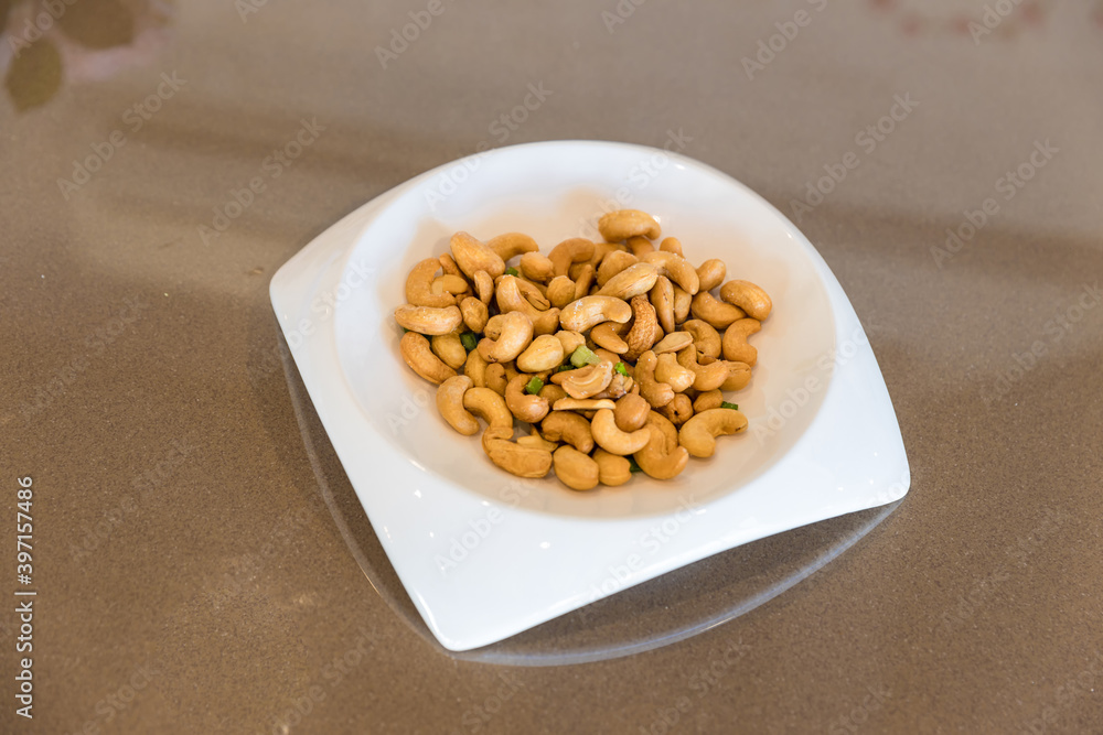 Tasty cashew nuts in plate on wooden table. white plate with cashew nuts on wooden table. Roasted cashew nuts Tasty cashew nuts in plate on wooden table. white plate with cashew nuts on wooden table. Roasted cashew nuts