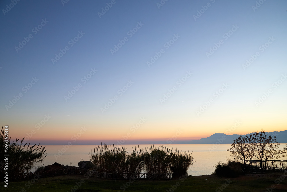 Obraz premium View from the embankment on water of sea and pink and yellow sunset on horizon in background