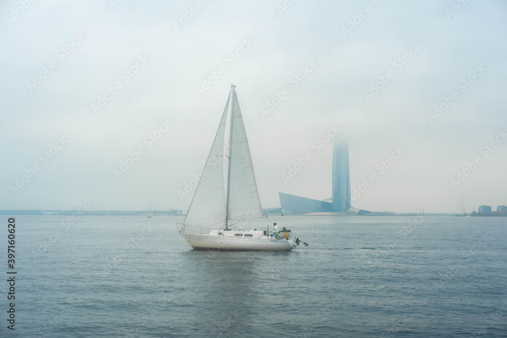  Sailboat in the waters of the Gulf of Finland. Saint-Petersburg, Russia. Foggy cloudy day, blue sky with low clouds and blue water.