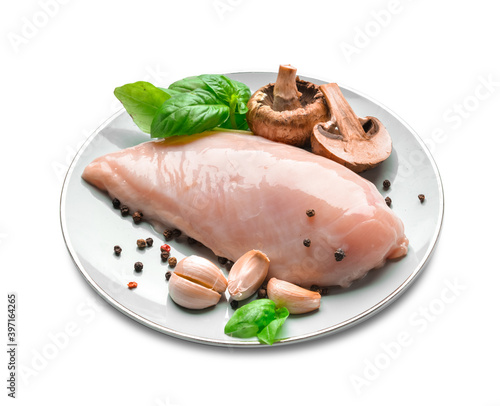 Plate with raw chicken fillet, mushrooms and garlic on white background