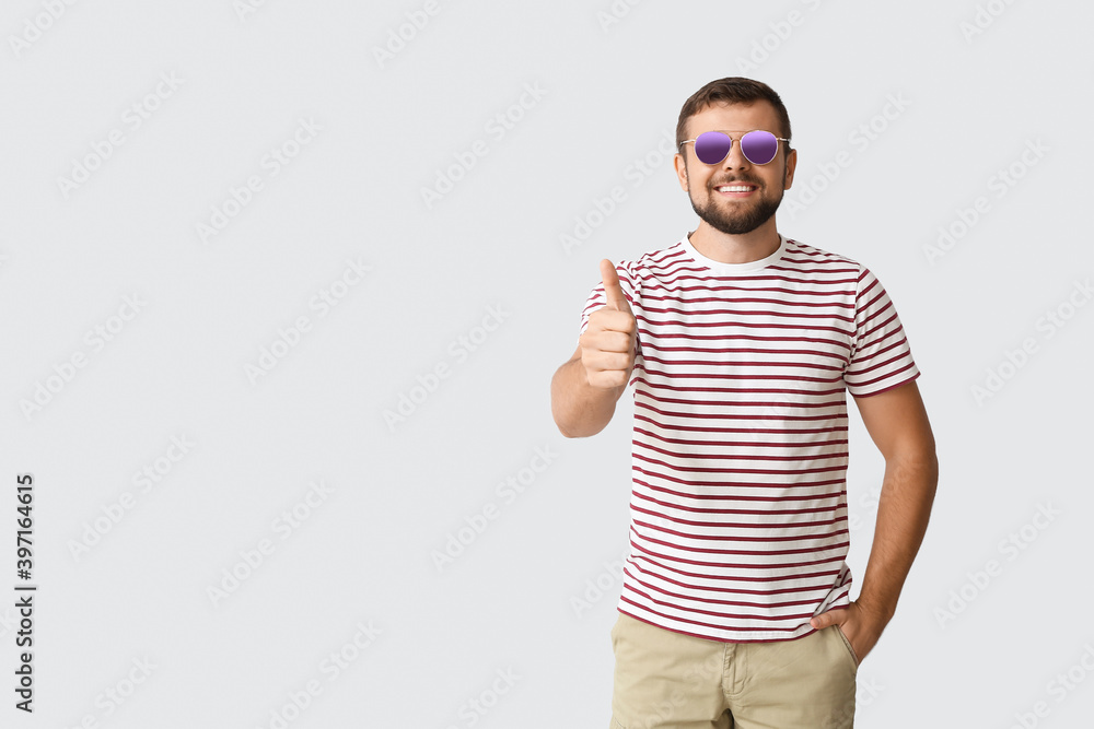 Handsome man with stylish sunglasses showing thumb-up gesture on light background Handsome man with stylish sunglasses showing thumb-up gesture on light background