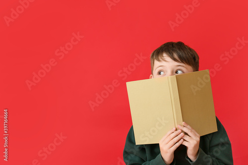 Cute little boy in autumn clothes and with book on color background © Pixel-Shot