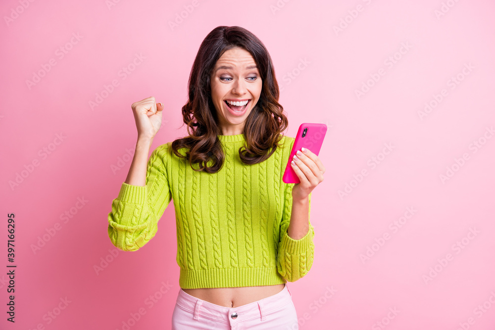 Photo of sweet wavy lady wear green sweater looking holding modern device rising fist isolated pink color background Photo of sweet wavy lady wear green sweater looking holding modern device rising fist isolated pink color background
