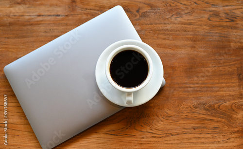 White coffee mug placed on the laptop on a wooden table.