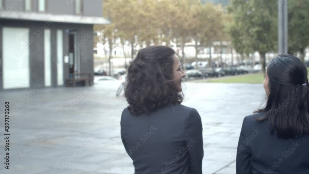Rear view of female coworkers going from work and talking. Successful experienced businesswomen discussing project outside and walking on street. Tracking camera. Business and communication concept
