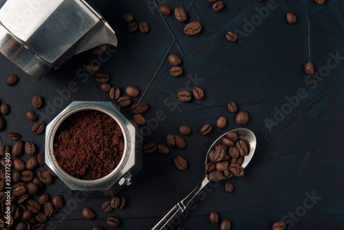 Metal spoon with coffee beans and coffee maker on dark textured background. Top view. Copy space.