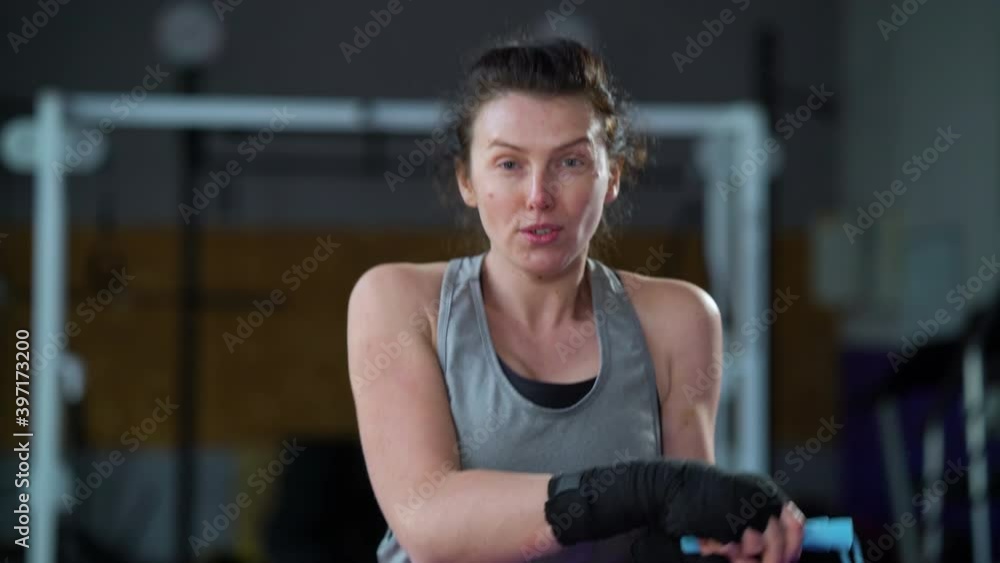 Athletic woman with bandages on hands training with skipping rope in gym and looking at camera, blurred background. Female boxer warming up. Concept of sport Athletic woman with bandages on hands training with skipping rope in gym and looking at camera, blurred background. Female boxer warming up. Concept of sport