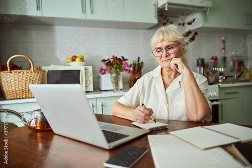Canvas Print Displeased old woman working on laptop at home