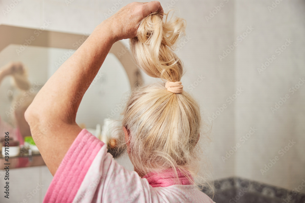 Fototapeta premium Senior woman holding her ponytail in bathroom