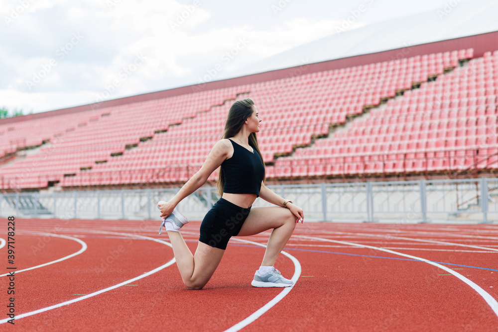 A female coach with dark hair stands on the red running track of the stadium