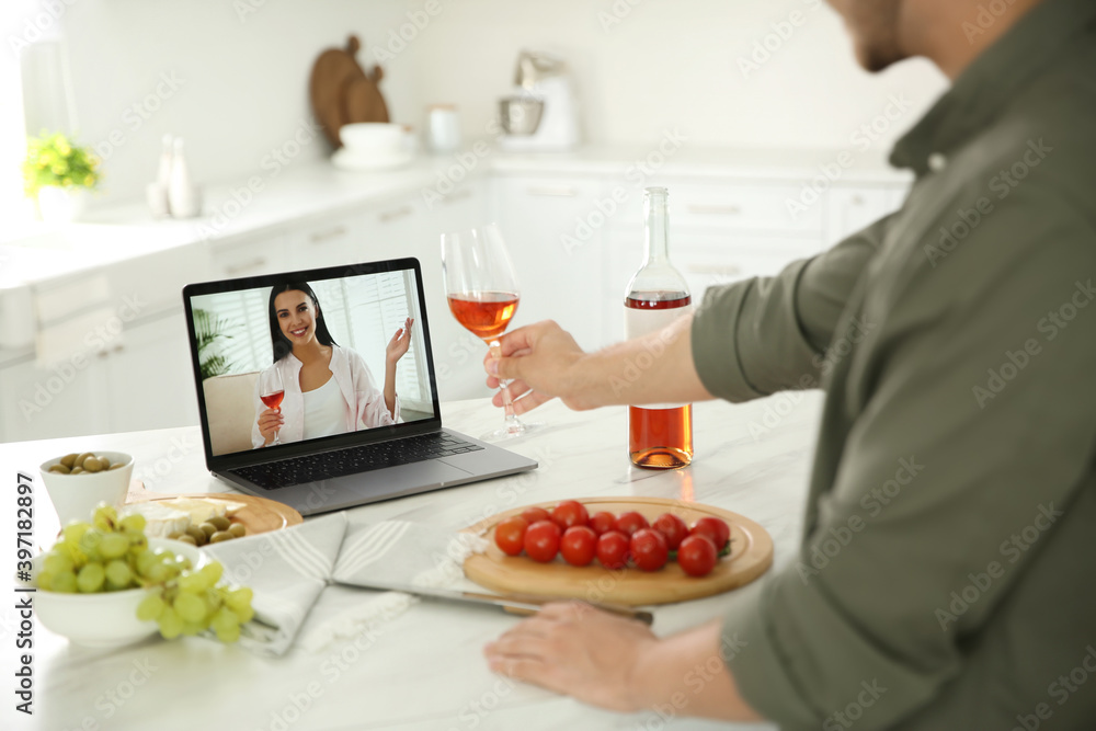 Friends drinking wine while communicating through online video conference in kitchen. Social distancing during coronavirus pandemic