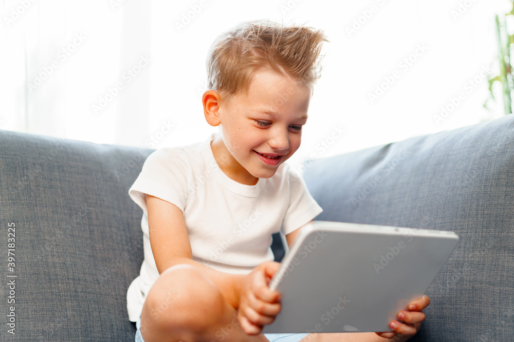 Little boy sitting on sofa and using digital tablet at home Little boy sitting on sofa and using digital tablet at home