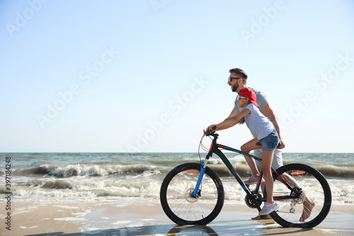 Happy father teaching daughter to ride bicycle on sandy beach near sea
