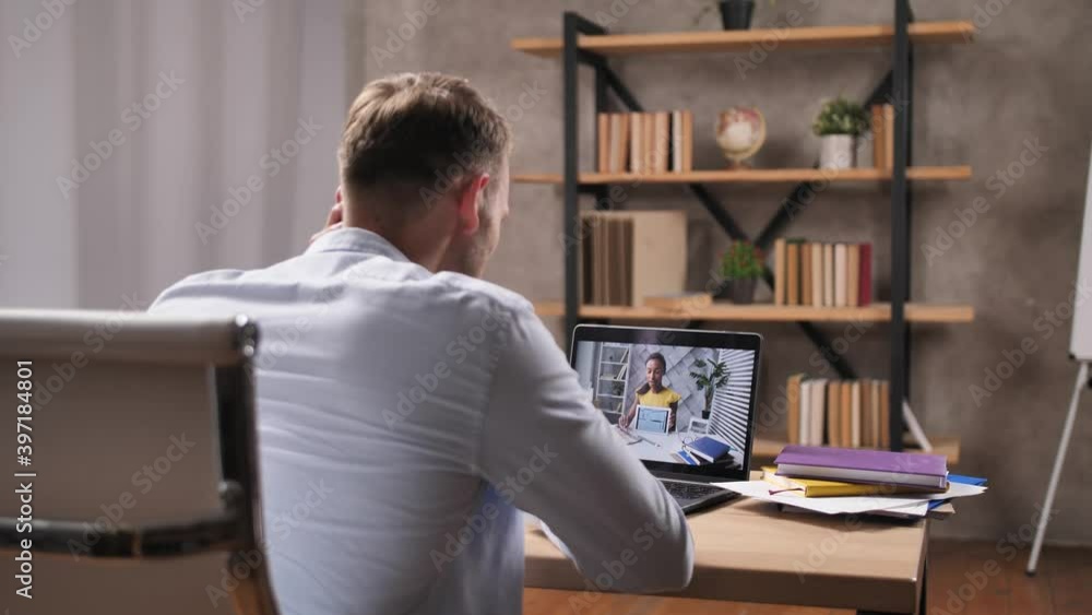 Rear view of young man meeting remotely with mixed race female interior designer during discussion of apartment renovation. Customer of redevelpment project conversating on laptop with woman designer Rear view of young man meeting remotely with mixed race female interior designer during discussion of apartment renovation. Customer of redevelpment project conversating on laptop with woman designer