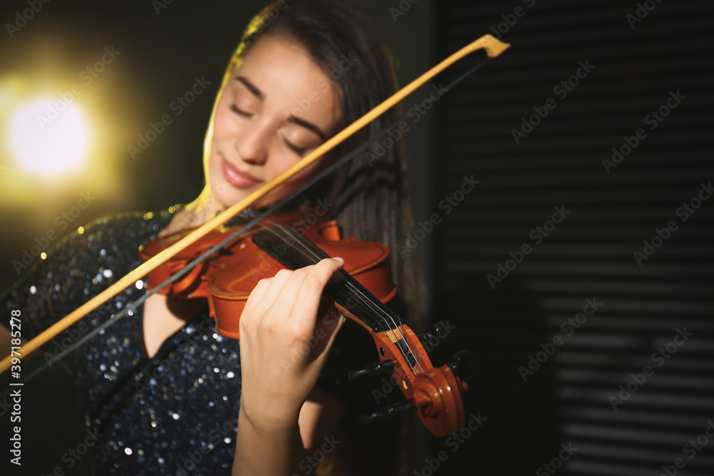 Fototapeta premium Beautiful young woman playing violin in dark room, focus on hand