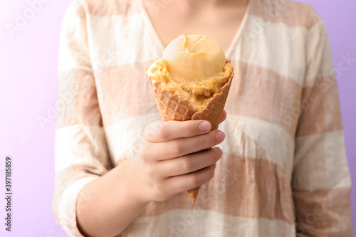 Woman holding yellow ice cream in wafer cone on violet background  closeup
