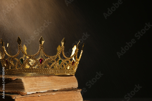 Beautiful golden crown and old books on black background, space for text. Fantasy item