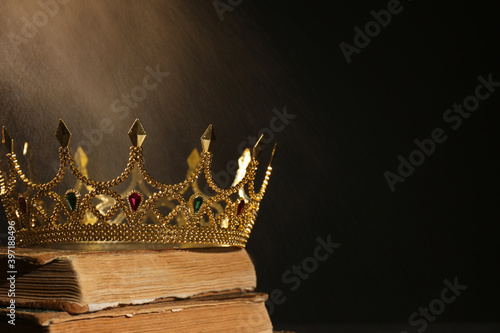 Foto Beautiful golden crown and old books on black background, space for text