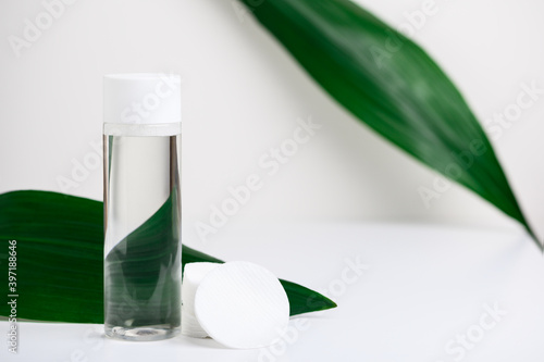 Makeup remover in plastic white bottle on a white background with green leaves, cotton cosmetic pads. Natural organic beauty liquid product. Micellar water for cleansing and moisturizing facial skin. photo