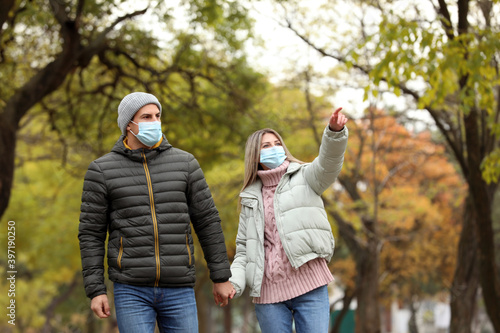 Couple in medical masks walking outdoors on autumn day. Protective measures during coronavirus quarantine