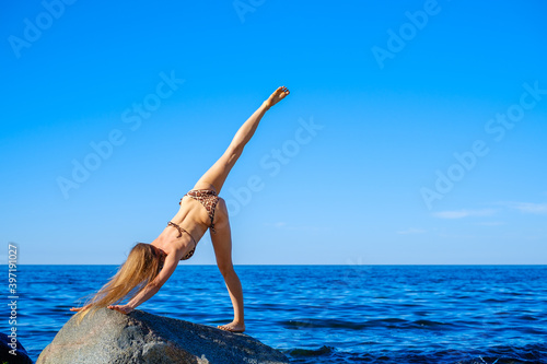 Slim female doing yoga against bright blue sky photo