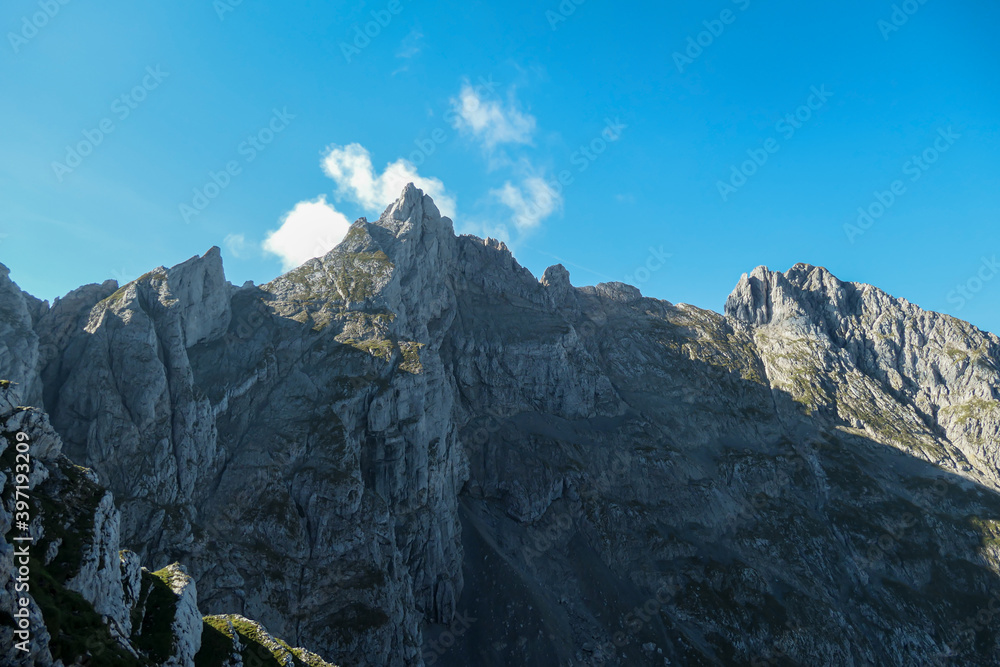 A panoramic view on Alpine slopes in Austria. There are sharp ans steep mountains and high peaks around. The Alpine slopes are almost barren, just moss overgrowing the slopes. Serenity and freedom.