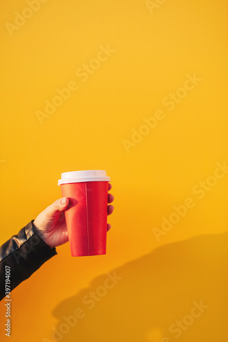 Paper cup of coffee in the hand of a young girl close up on a yellow background