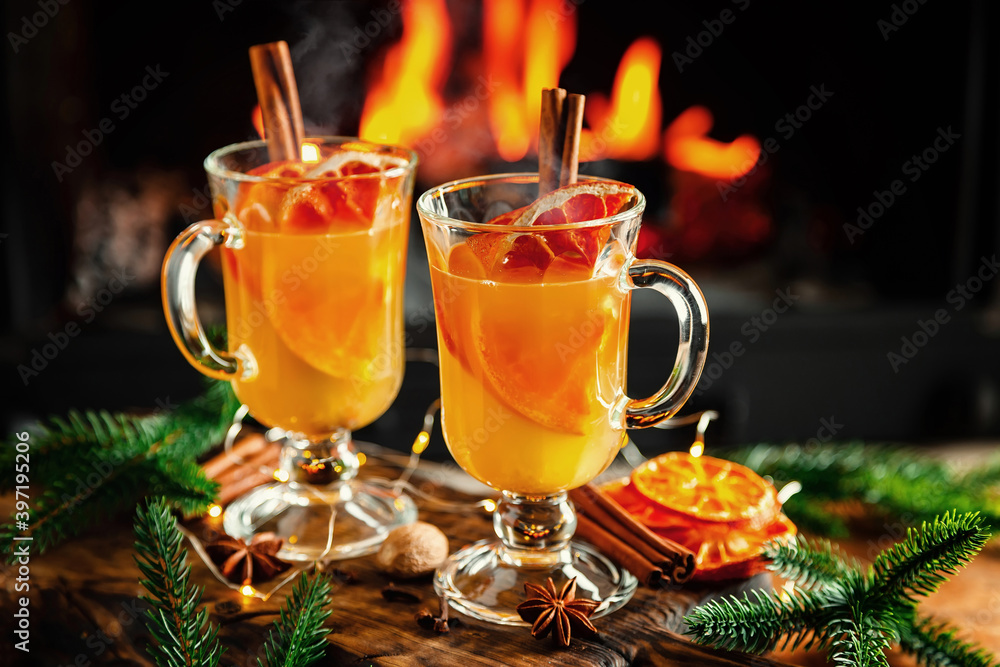 Mulled cider glasses on the background of fireplace fire. Hot mulled spiced apple cider cocktail for winter or autumn time. Mulled cider glasses on the background of fireplace fire. Hot mulled spiced apple cider cocktail for winter or autumn time.