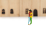 Miniature people standing hugging and kissing each other, the background of the house is blurry.