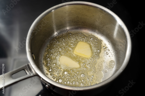 Fotografie Melting butter in a stainless steel saucepan on the black stove, cooking concept