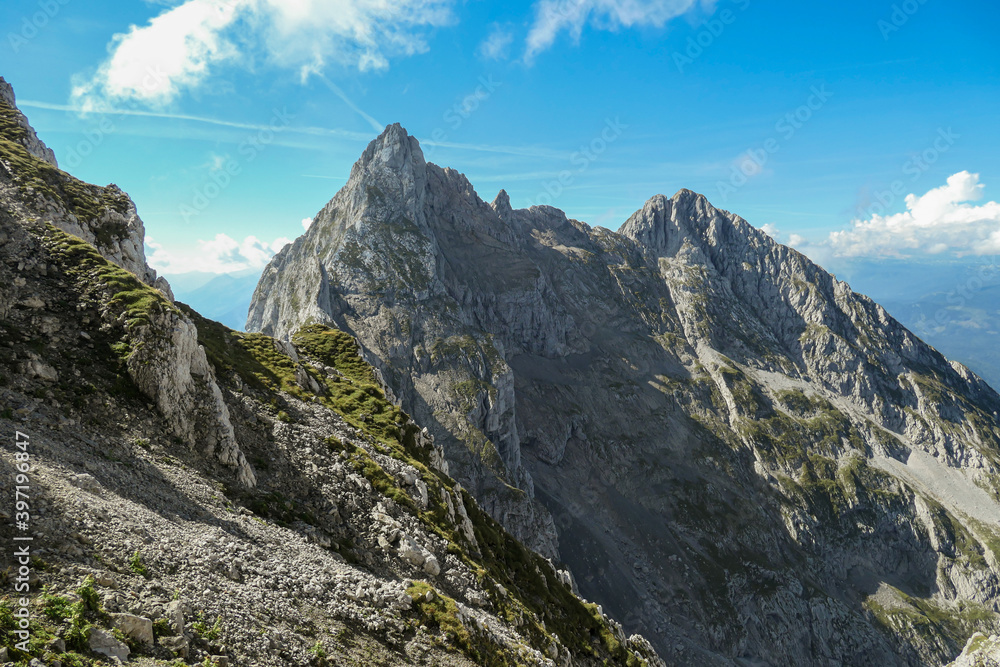 A panoramic view on Alpine slopes in Austria. There are sharp ans steep mountains and high peaks around. The Alpine slopes are almost barren, just moss overgrowing the slopes. Serenity and freedom.