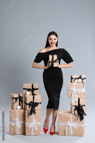 Woman in black dress with Christmas gifts on grey background