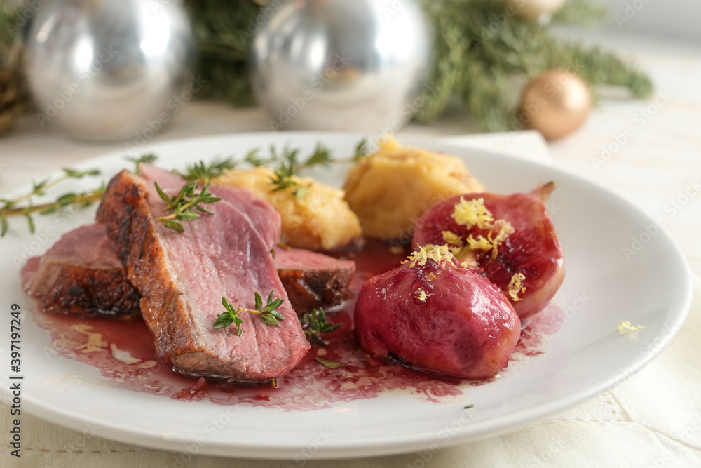 Festive holiday dinner, roasted duck slices with fig, mashed parsnip and red wine sauce on a white plate, Christmas decoration in the background, close up shot, selected focu Festive holiday dinner, roasted duck slices with fig, mashed parsnip and red wine sauce on a white plate, Christmas decoration in the background, close up shot, selected focu