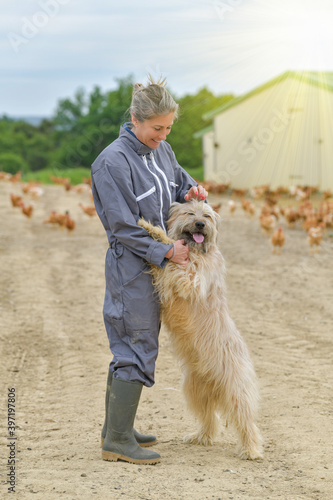 Portrait of a farmer petting her dog and standing in the middle of her chicken farm