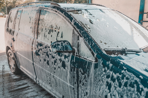 Car wash, a person at a self-service car wash, under a stream of pressure puts foam on the car. © Niko_Dali