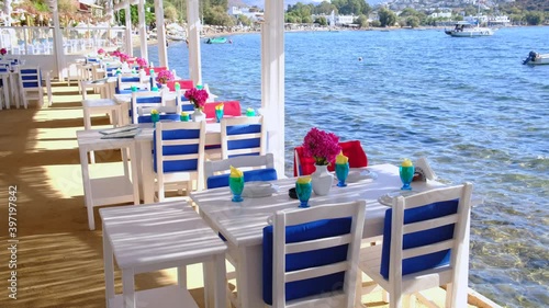 Aegean fish restaurant, tables and chairs with bougainvillea flowers next to see in Bodrum, Turkey at sunny day. It is very famous and attraction point for tourist in Bodrum.